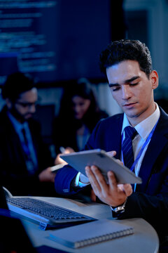 A data analyst scrolls through complex visualizations on a tablet comparing results against code displayed onscreen working late to finalize a critical business intelligence report.