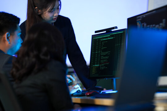 Night sprint sync up. Standing team lead points out critical code section screen seated developers listen focused collaborative problem solving agile workflow tech startup vibe. - Powered by Adobe