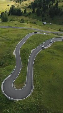 Vertical screen Drone shot dramatic hairpin mountain pass with multiple cars hugging curves, rally driver testing performance on alpine asphalt while camera drone traces every turn.
