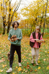 In a vibrant autumn forest, a couple collects firewood. The ground is covered in colorful fallen...