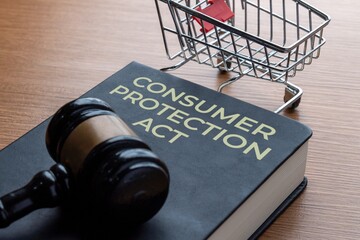 A gavel on a book titled CONSUMER PROTECTION ACT with a miniature shopping cart. Legal rights, retail safety, law, justice, and customer defense concept.