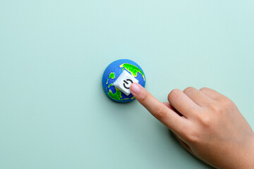 Hand pressing power button on a small Earth model. Earth Hour, global energy saving, environmental awareness, climate action concept.