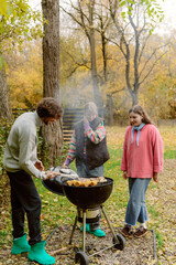 Friends gather outdoors to enjoy a barbecue on a sunny autumn day. The scene is filled with laughter, smoke from the grill, and colorful fall leaves surrounding them.