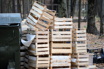 Stacked wooden crates placed beside a large waste container in an outdoor setting. Concept of storage, logistics, recycling, and waste management in an industrial or agricultural environment.