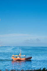 Naklejka premium Vintage Wooden Sailboat Sailing on the Calm Blue Ocean Water with a Clear Blue Sky