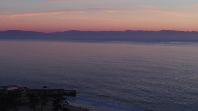 A beautiful and colorful ocean sunset seen from Santa Cruz California state beach looking over the pacific ocean towards Monterey California in a serene panning aerial drone shot with waves crashing