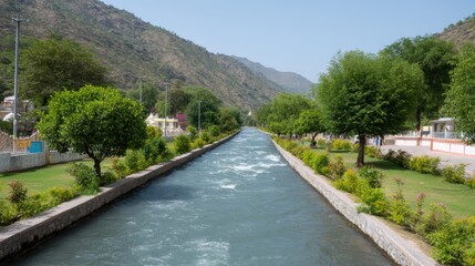 Fototapeta premium Serene River Flowing Through Green Landscape in Mountainous Region Under Clear Blue Sky with Lush Trees and Well-Maintained Pathways