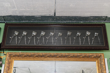 A framed display of vintage manual hair clippers arranged in a row above a decorative mirror in a classic barbershop setting.