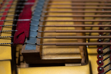 Close-up of the internal string mechanism of a piano, showing coiled copper-wound bass strings, metal pins, and red felt dampers in fine detai