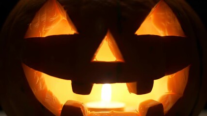 Illuminated Jack-o'-lantern with candle glowing, Halloween pumpkin carving with scary face.