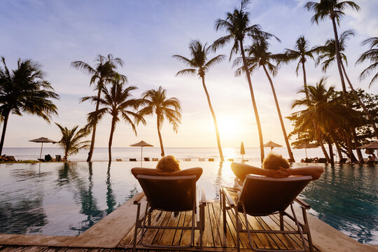 honeymoon couple on vacation in luxury beach hotel, man and woman relaxing near swimming pool at sunset