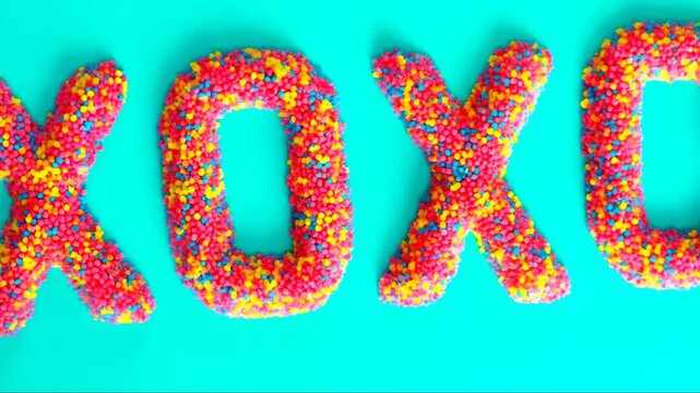 XOXO Hugs and Kisses Text Made of Colorful Candy Sprinkles Zooming In on Turquoise Background