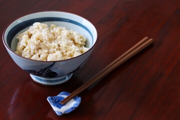 Close up shot of freshly cooked brown rice in traditional Japanese rice bowl with wooden chopsticks on wooden table.
