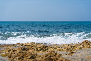 A stunning seascape featuring vibrant azure waves crashing against a rugged shoreline. The scene is set under a clear blue sky, ideal for travel brochures and coastal decor projects.