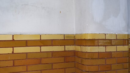A horizontal architectural detail of a wall featuring a white plastered top section above several rows of glossy yellow and orange bricks with visible masonry grout lines.