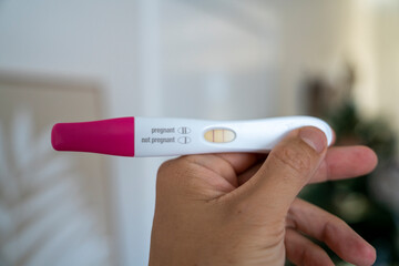 Hand holding pregnancy test showing positive result indoors