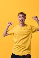 Fototapeta premium Cheerful man in a yellow shirt raises his arms in celebration against a bright yellow background, radiating energy and positive mood.