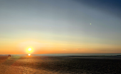 The breathtaking sunset beautifully reflects on the calm ocean, creating a truly serene beach atmosphere