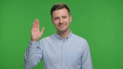 friendly young man giving a polite greeting with a raised hand against a green screen background