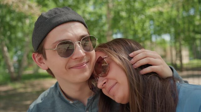 romantic pair resting under sunlight, young couple relaxing together beneath gentle sunlight and shade, affectionate young partners sitting close on park bench amidst warm sunlight and nature