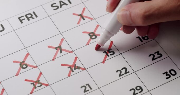 Hand marking off days in a calendar with a red marker. Concept of scheduling, planning, and time management. Highlighting important dates and tracking progress.