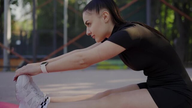 A focused young woman in athletic wear stretches her hamstring on a yoga mat in a park, showcasing a healthy lifestyle and fitness routine. Young Woman Performing Hamstring Stretch at Outdoor Park