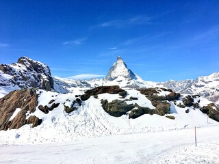 The famous Matterhorn peak rising above rocky foreground and snow-covered slopes on a sunny winter day in Zermatt.