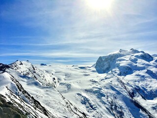 Sun shining brightly over the snow-capped Breithorn mountain range and glaciers in the Swiss Alps, high contrast silhouette.