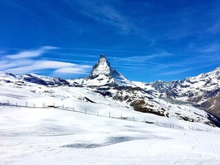 Winter landscape in Zermatt featuring the Matterhorn mountain, ski slopes, and railway fences under a clear blue sky