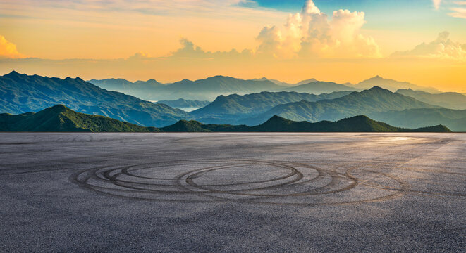 Empty asphalt road square with tire tracks and beautiful mountain range landscape at golden sunset