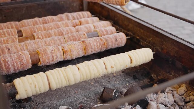 Chimney cakes browning evenly on hot rollers with crisp crust forming in warm shop lighting