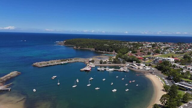 Aerial of Ulladulla Harbour with boats, calm blue water, and coastal town surrounds, establishing orbit
