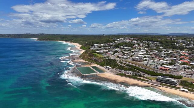 Aerial tracking Merewether coastline showing beach and rocky edges with open water pool baths at center