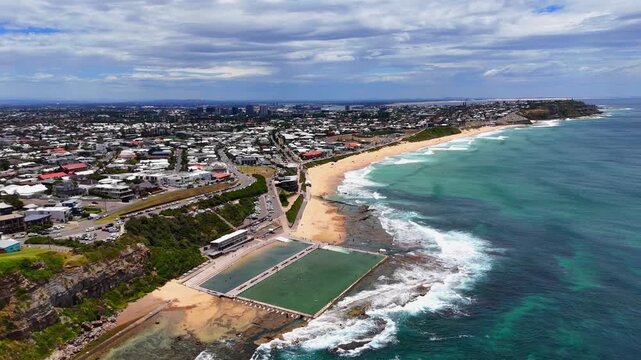 Wide aerial panorama of Merewether Beach and pool curving along the Newcastle coastline, orbit establish