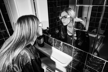 Drunken woman touching her face, looking at her reflection in a bathroom mirror