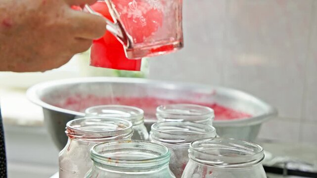 woman filling glass jars with fresh strawberry jam in domestic kitchen
