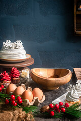 A cozy holiday atmosphere unfolds as baking begins, with a wooden bowl surrounded by eggs, cupcakes, Christmas decorations, and various ingredients—perfect for a Christmas and New Year's cooking theme