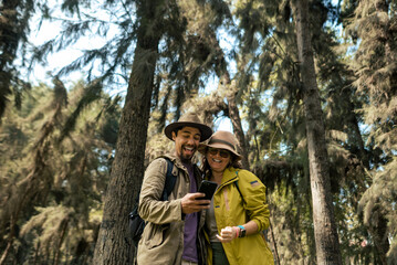 Fototapeta premium A couple of tourists look at their phone happily in the middle of the forest. Travel concept