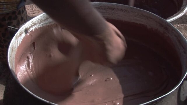 Close-up of a woman&rsquo;s hand vigorously kneading thick brown shea butter paste in a large metal basin during traditional processing in northern Ghana.
