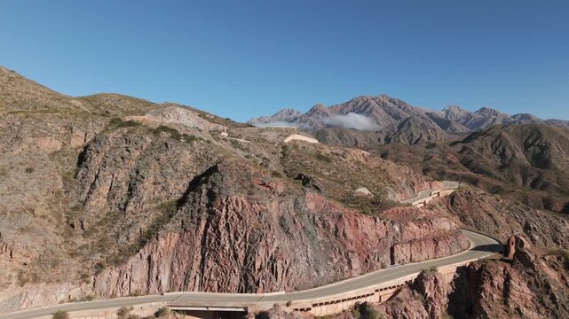 Drone gliding over Cuesta de Miranda mountain pass on Route RN 40 in La Rioja, Argentina, highlights winding road carved into the steep reddish-brown rock formations of the Sierras Pampeanas
