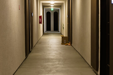 Obraz premium Empty apartment hallway at night with warm lighting, exit sign, and clean concrete floor, creating a quiet, minimal residential interior scene.