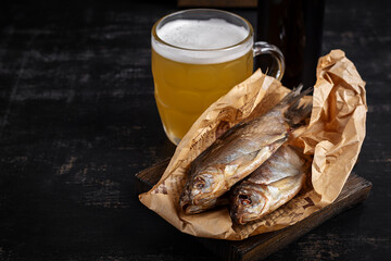 Dried roach fish and glass of beer on dark table, close up