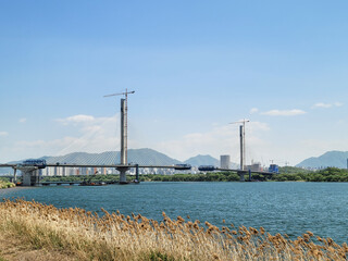 SEOUL, SOUTH KOREA - MAY 2024: Construction of a new cable-stayed bridge over the Han River with cranes and mountains in the background.