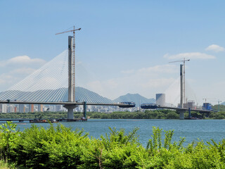 SEOUL, SOUTH KOREA - MAY 2024: Construction of a new cable-stayed bridge over the Han River with cranes and mountains in the background.