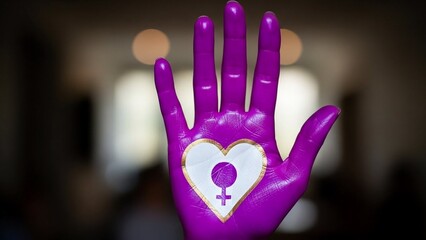 Vibrant purple sculpted hand featuring a prominent heart shaped symbol of feminism, set in a softly blurred indoor environment