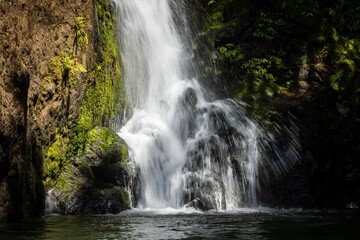 Fototapeta premium Scenic waterfall flowing down a rock face covered in green moss and plants. The water creates a refreshing and peaceful atmosphere in nature.