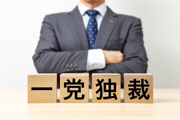 「一党独裁」と書かれたブロックと腕組みをするビジネスマン