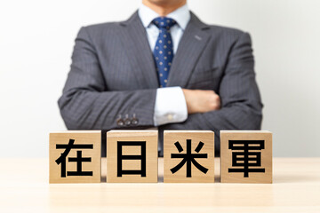 「在日米軍」と書かれたブロックと腕組みをするビジネスマン