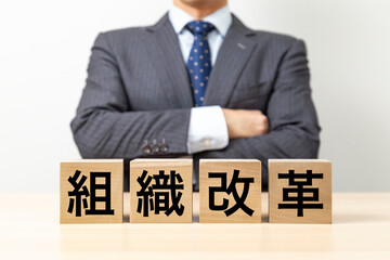 Obraz premium 「組織改革」と書かれたブロックと腕組みをするビジネスマン