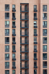 Fototapeta premium Full Frame Shot Of A Multi Story Brick Residential Building. The Regular Pattern Of Windows And Balconies Creates An Architectural Texture.